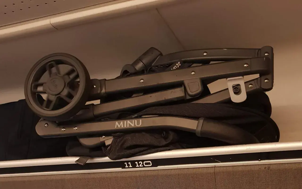 En hopfälld barnvagn, märkt "MINU", ligger som handbagage på en hylla.