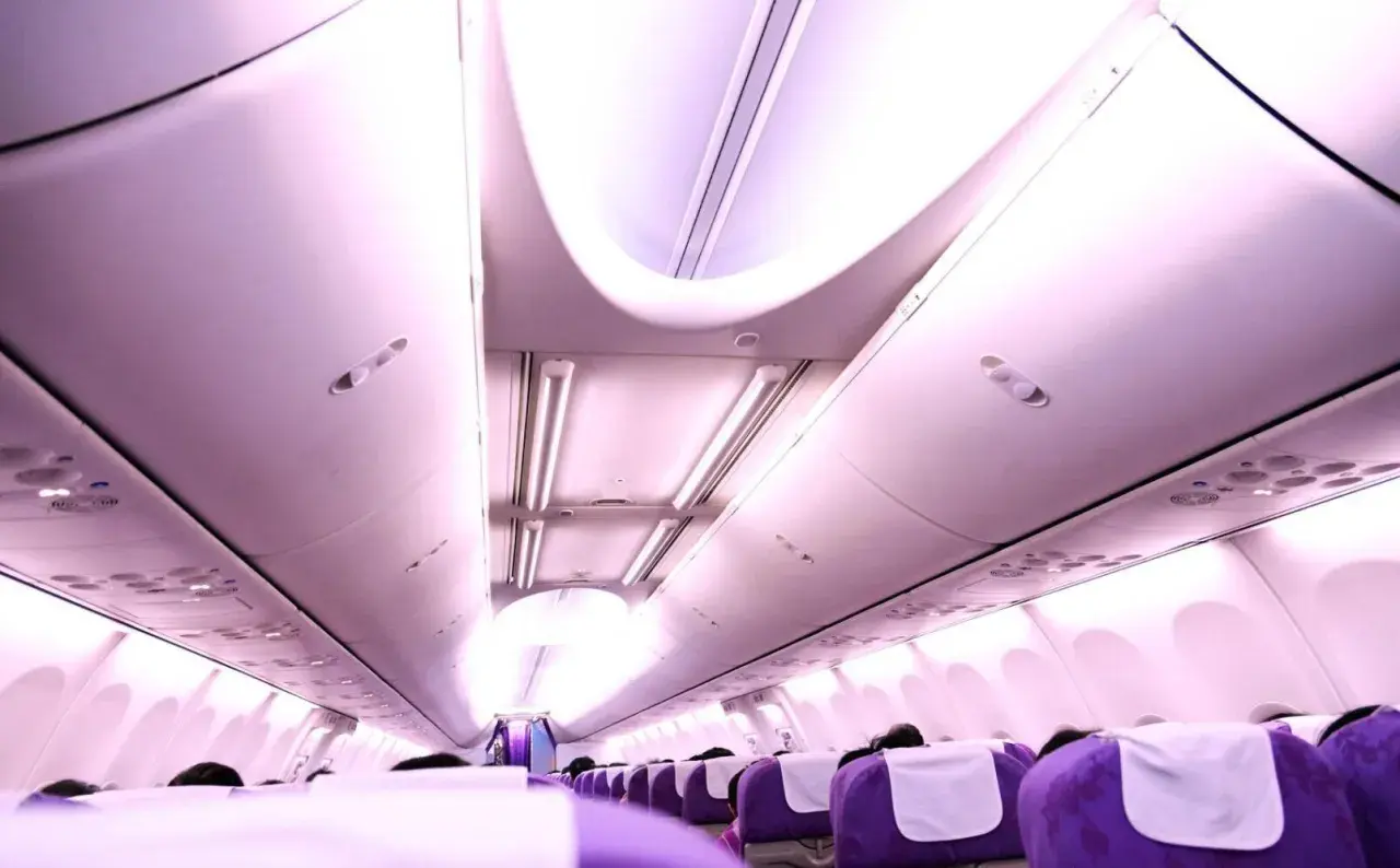 Rad av lila ving flygplan sittplatser med vita nackstöd, belysta av taklampor.