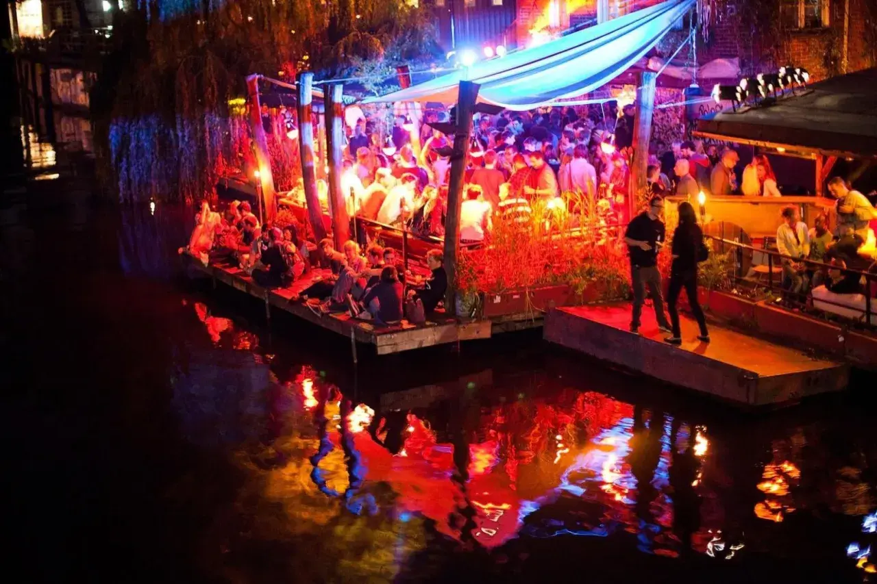 Folk festar på en flytande nattklubb i Berlin. Ljusen reflekteras i vattnet.