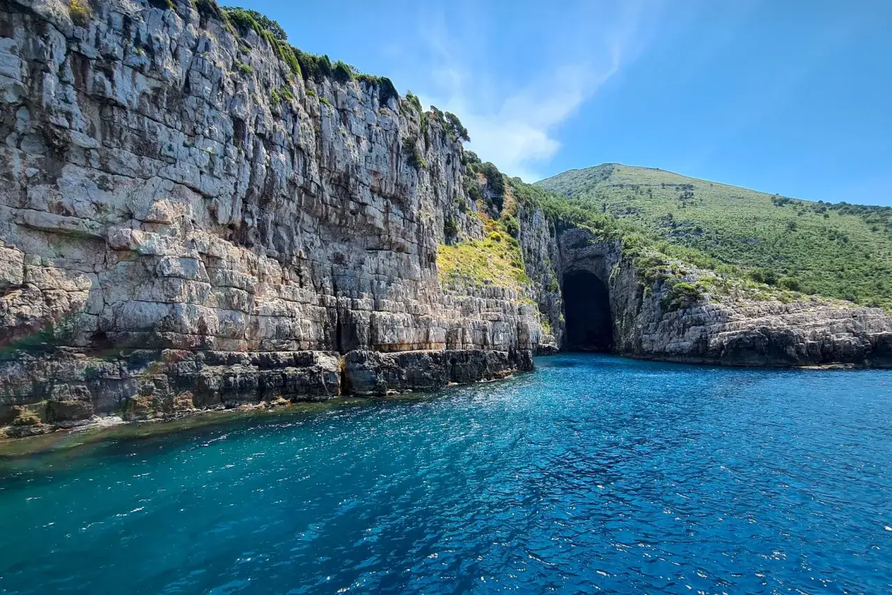 Bl&aring;gr&ouml;nt vatten leder in mot en grotta mellan h&ouml;ga klippor. Ett fantastiskt albanien resm&aring;l med dramatiska vyer.