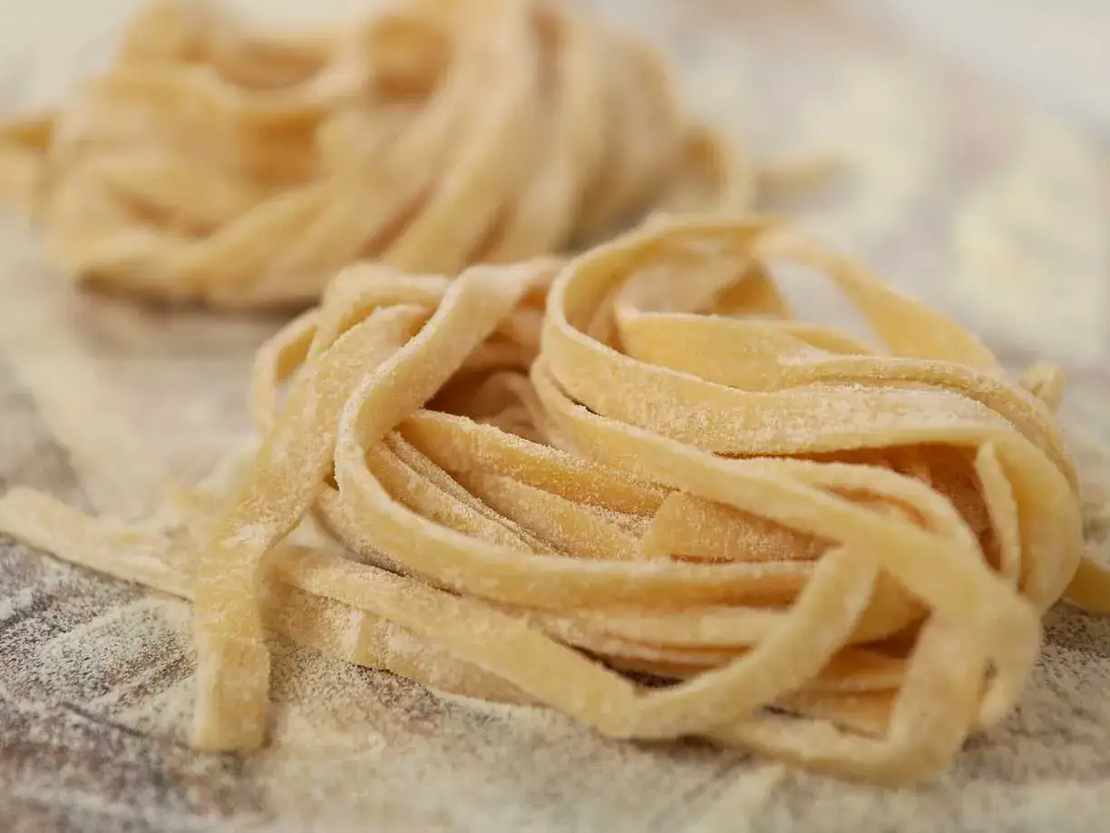 F&auml;rska, hemgjorda nudlar som ser ut som ett perfekt pastadeg recept. De ligger i mj&ouml;l p&aring; en tr&auml;yta.