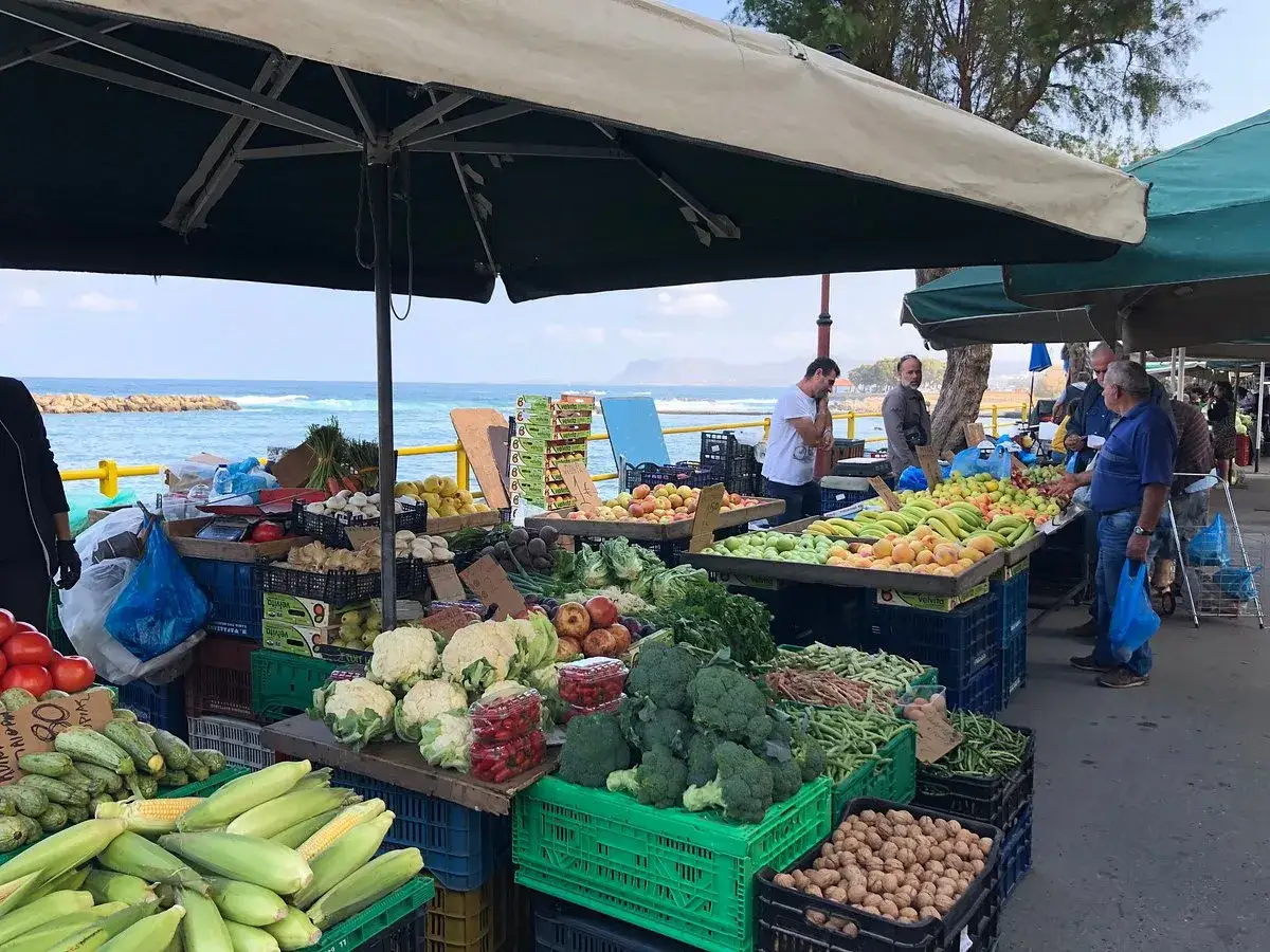 Frukt och gr&ouml;nsaker p&aring; en livlig marknad i Chania, med havet som bakgrund.