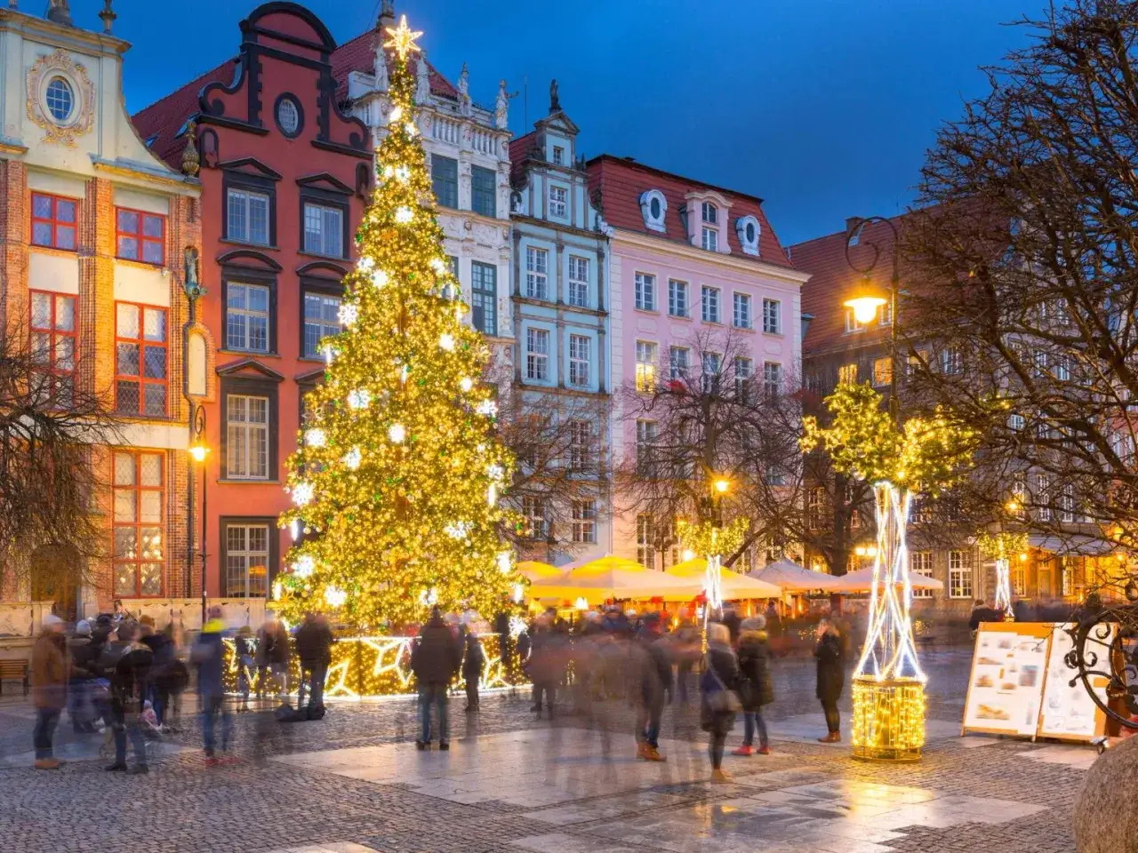En magisk julmarknad i Gdansk med ett glittrande julgransljus och folk som njuter av den festliga st&auml;mningen bland f&auml;rgglada hus.