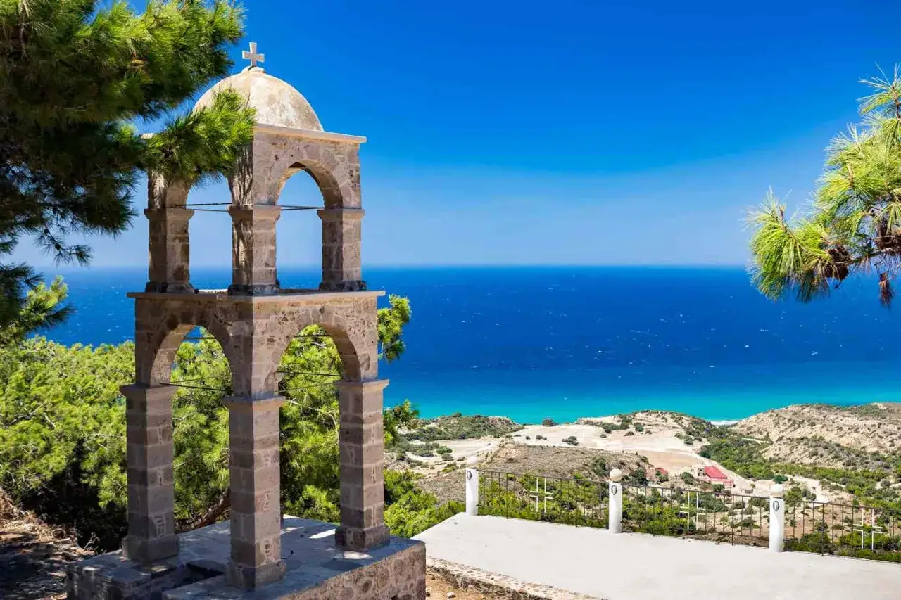 Stenklocktorn med kupol och kors, blickar ut &ouml;ver det azurbl&aring; havet vid kos stad.