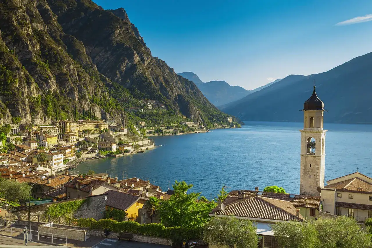 Vacker vy &ouml;ver en stad vid en sj&ouml; i norra Italien, med berg som reser sig bakom. En kyrka med klocktorn dominerar vyn.