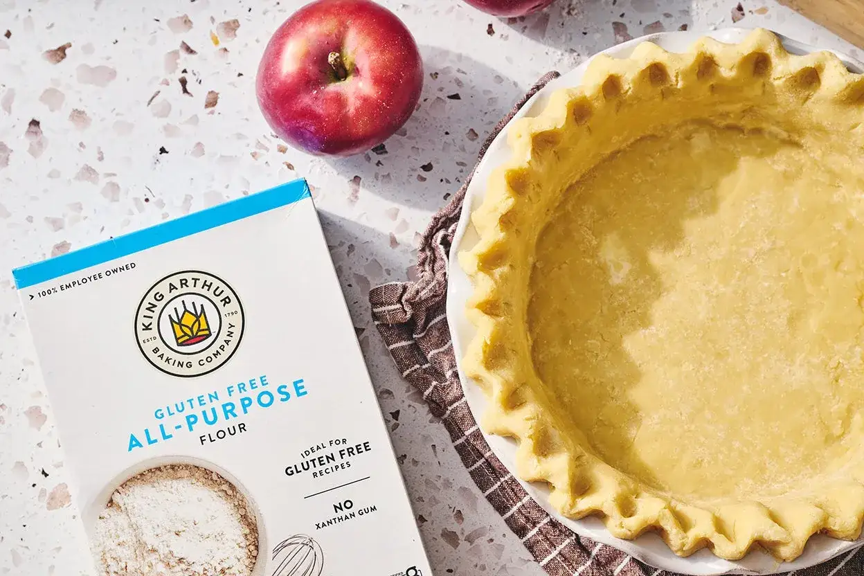 En f&auml;rdigbakad glutenfri pajdeg i en form, bredvid en l&aring;da med King Arthur Gluten Free All-Purpose Flour och r&ouml;da &auml;pplen.