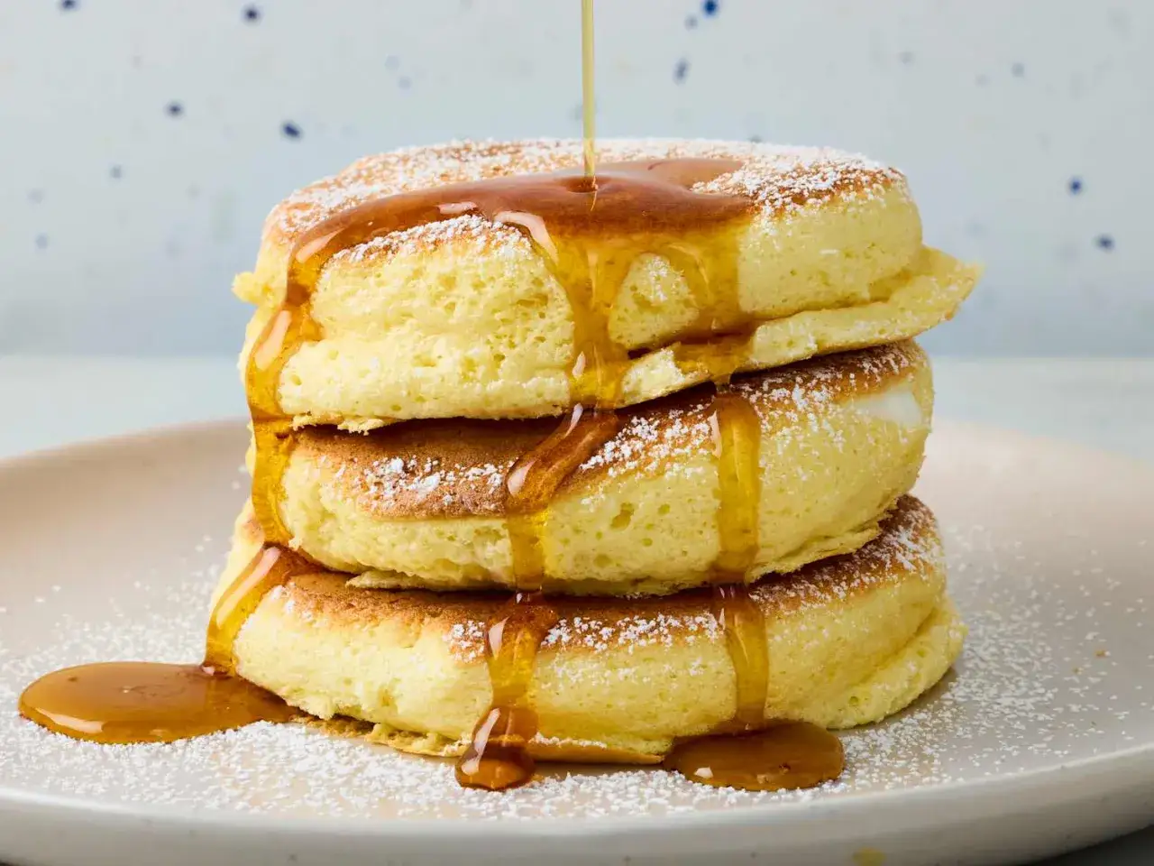 En stapel fluffiga japanska pannkakor, pudrade med florsocker och dr&auml;nkta i sirap.