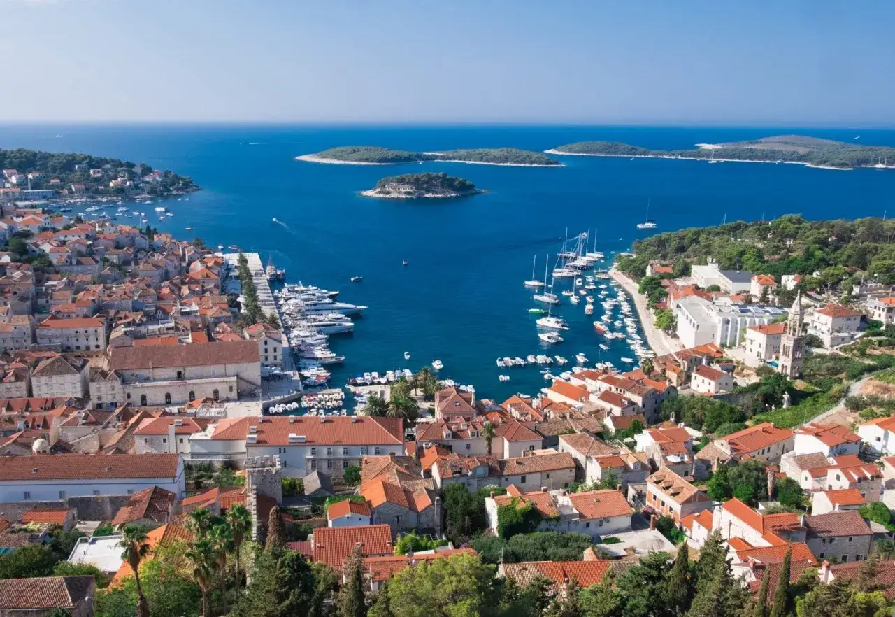 Vacker vy &ouml;ver Hvar, Kroatien, med r&ouml;da tak, en livlig hamn full av b&aring;tar och turkost hav med sm&aring; &ouml;ar.