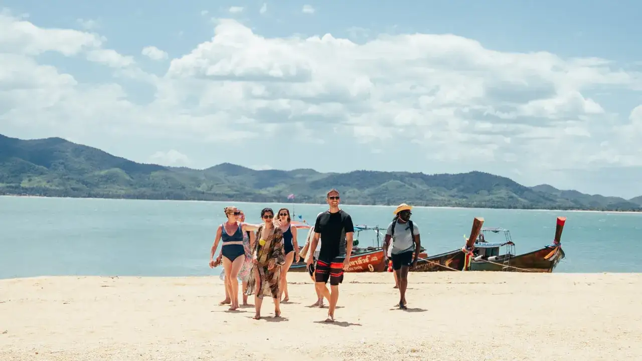En grupp v&auml;nner njuter av en solig dag p&aring; stranden. De verkar ha en h&auml;rlig resa ensam i grupp, med en traditionell longtailb&aring;t i bakgrunden.
