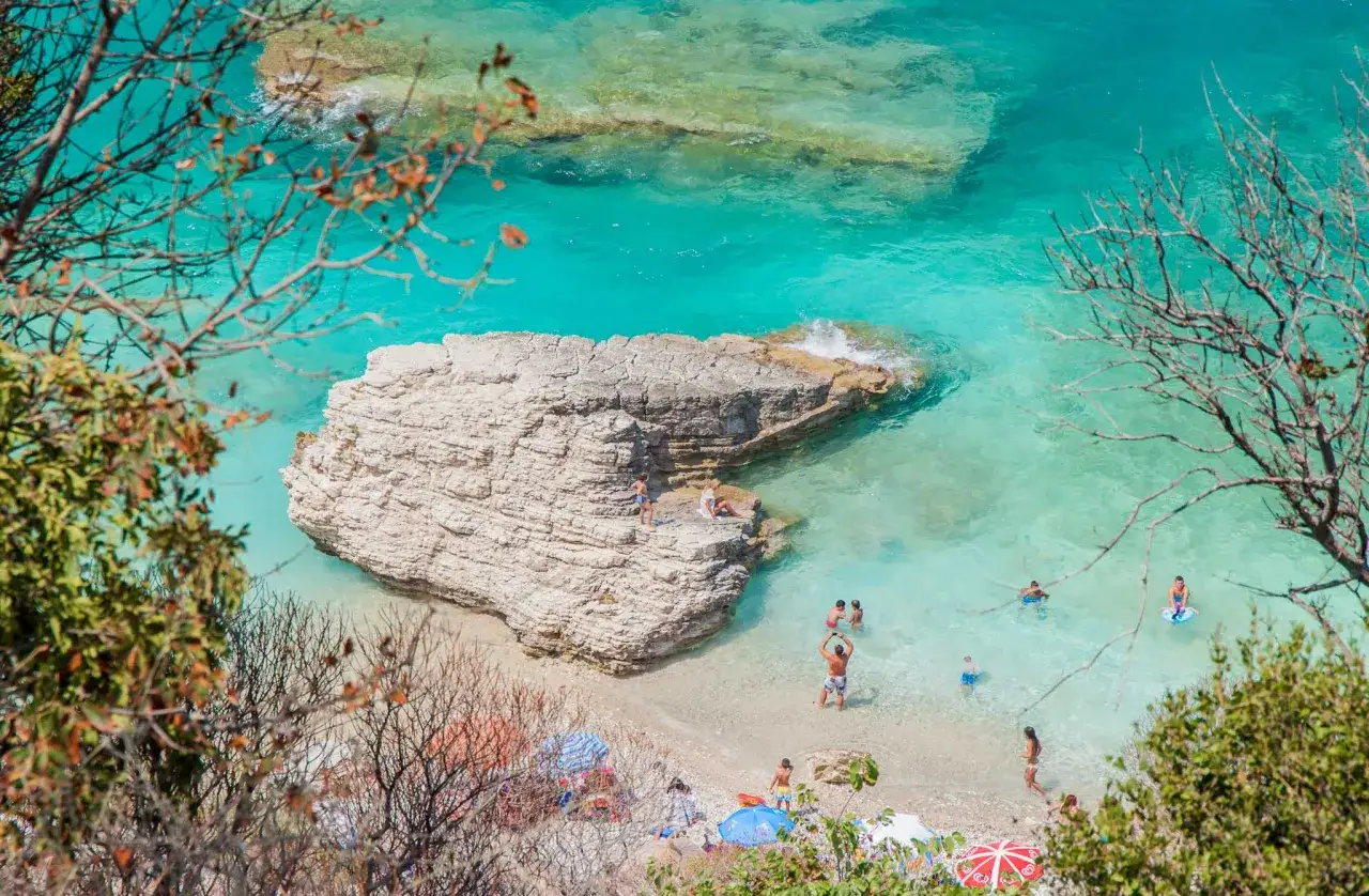 M&auml;nniskor njuter av det turkosa vattnet vid en klippig strand, en perfekt plats f&ouml;r att uppleva varmast i Europa.