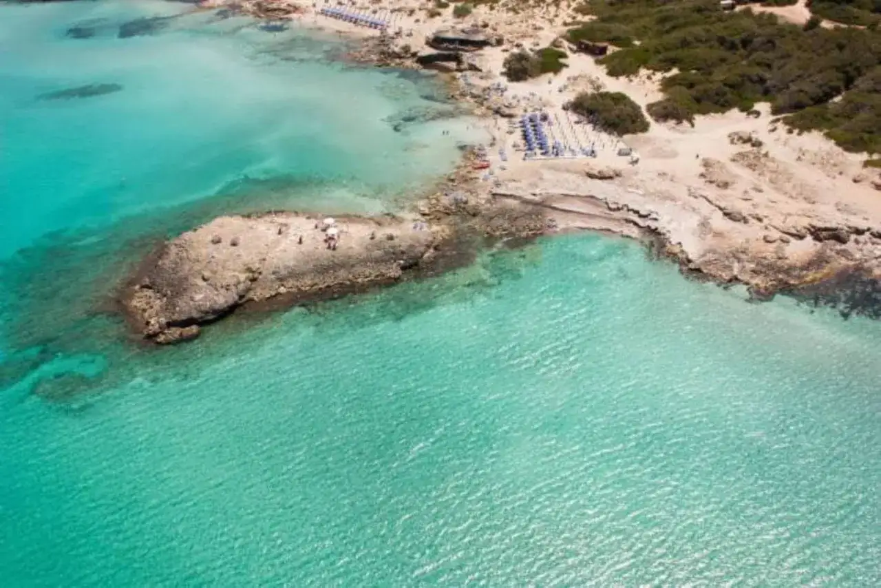 Turkost vatten och klippig kustlinje vid en strand i Salento, Italien. Solstolar och parasoller vittnar om en solig semester.