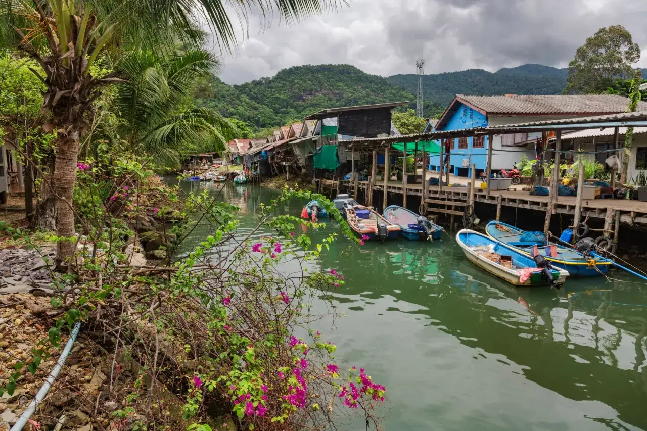 Fiskeb&aring;tar flyter i en kanal vid en liten by p&aring; Koh Chang. Palmer och bougainvillea kantar vattnet.