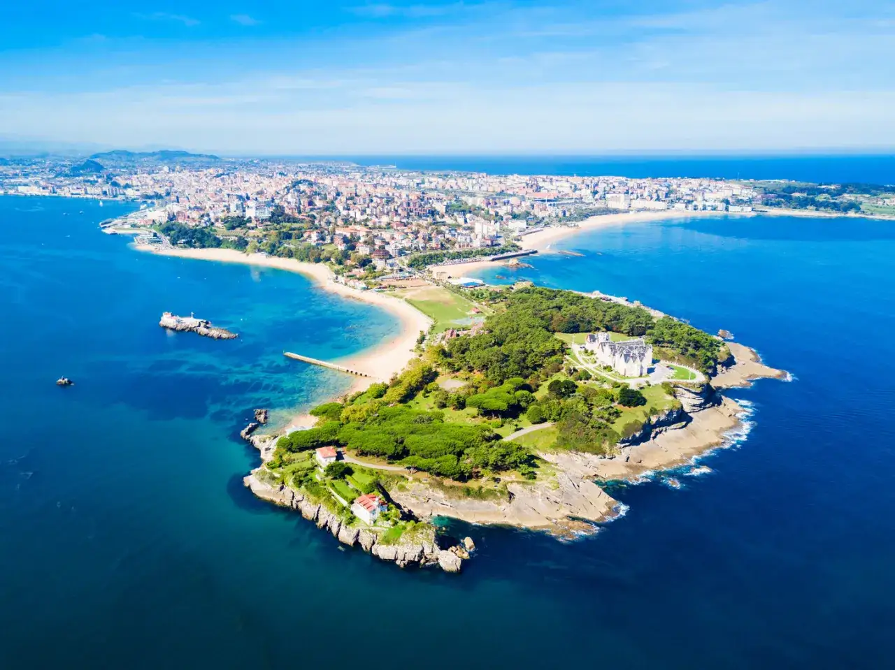 Vacker vy &ouml;ver Santander, Spanien, med en stad som str&auml;cker sig l&auml;ngs kusten och en gr&ouml;nskande halv&ouml; med ett st&aring;tligt slott.