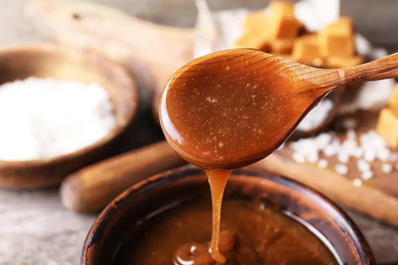 En sked med varm kolas&aring;s som droppar ner i en sk&aring;l. Ingredienser f&ouml;r ett kolas&aring;s recept syns i bakgrunden.