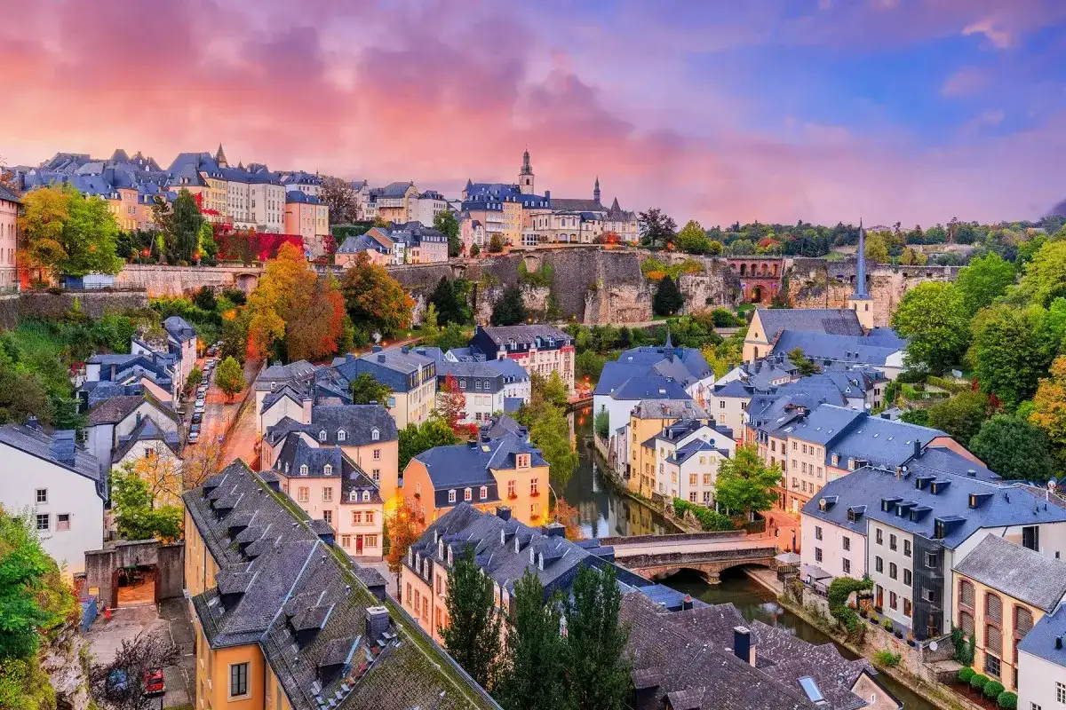 Vacker vy &ouml;ver Luxemburgs huvudstad med sina historiska byggnader och en flod som slingrar sig genom staden under en f&auml;rgsprakande solnedg&aring;ng.