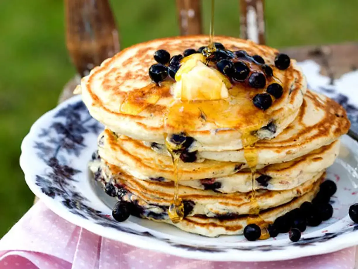 En h&ouml;g med fluffiga amerikanska pannkakor med bl&aring;b&auml;r, sm&ouml;r och sirap som rinner ner. Perfekt frukost!