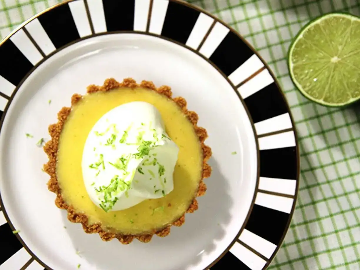 En l&auml;cker key lime pie med vispgr&auml;dde och rivet limeskal. En halv lime ligger bredvid p&aring; en rutig duk.