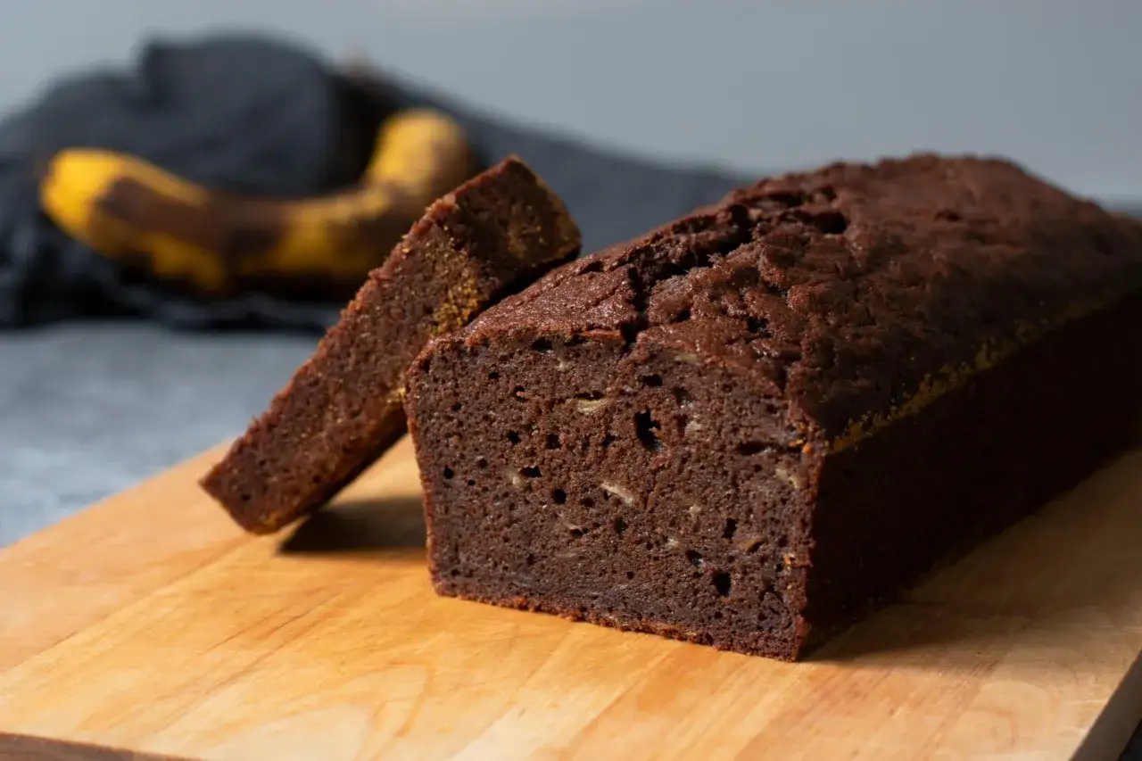En saftig banankaka med choklad, en skiva uppskuren. En &ouml;vermogen banan ligger i bakgrunden, redo att bli en del av n&auml;sta goda bakverk.
