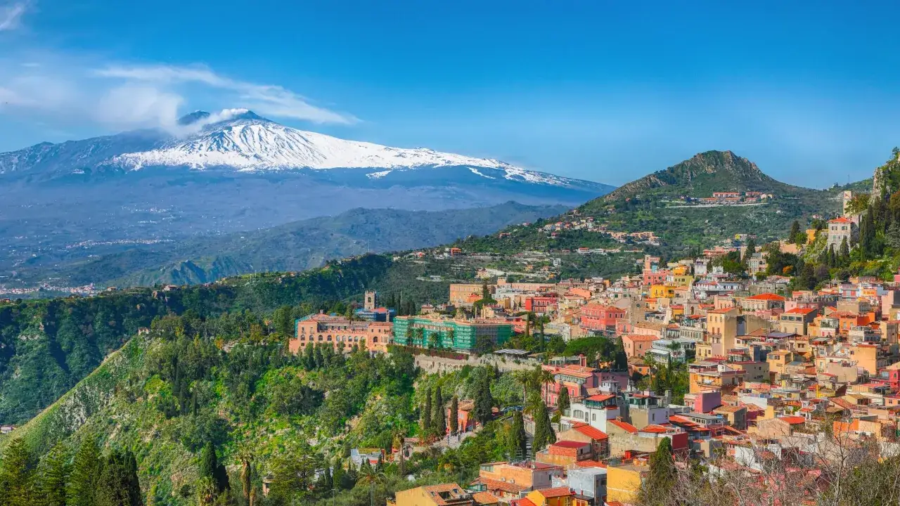 F&auml;rgstark stad med sn&ouml;t&auml;ckt vulkan i bakgrunden, en vy &ouml;ver Catania p&aring; Sicilien.