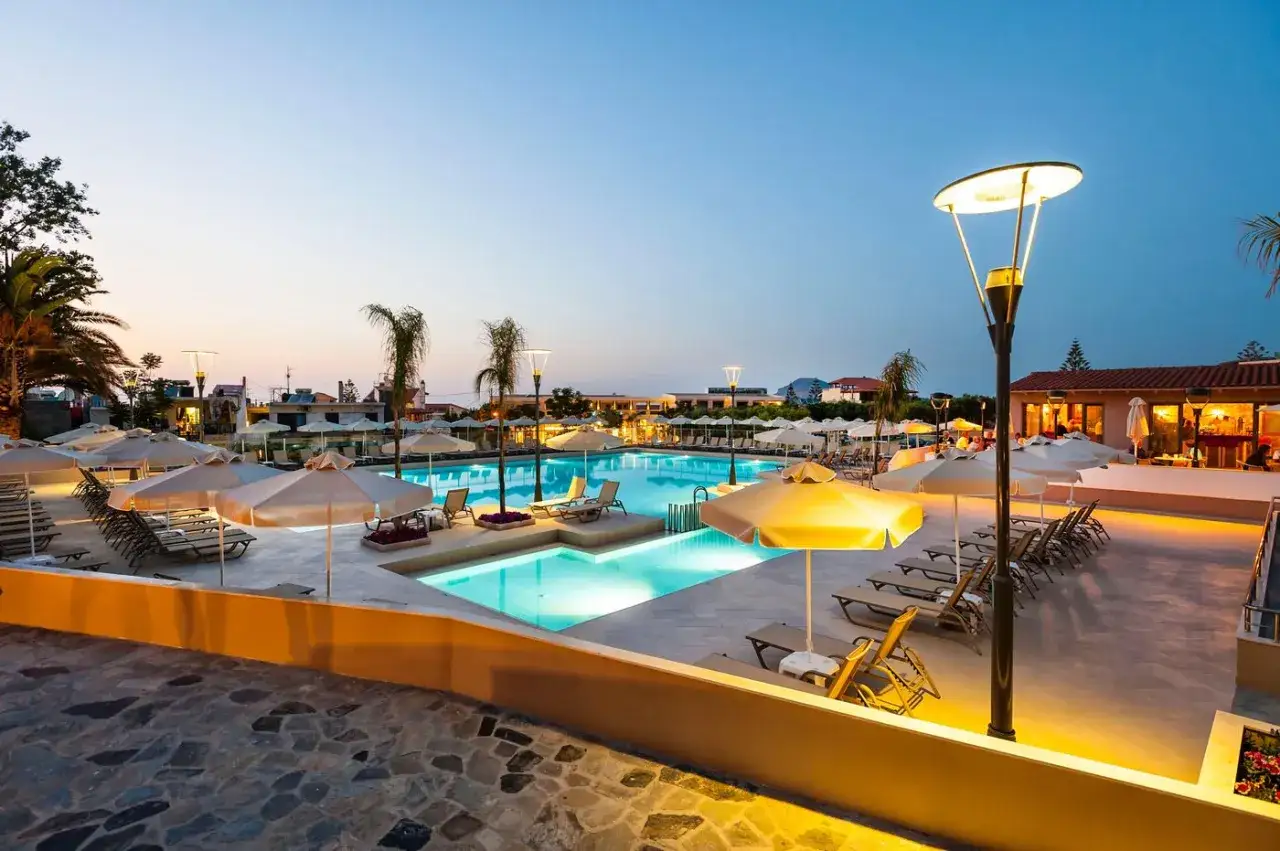 En vacker kväll vid poolen i Platanias, Kreta. Solstolar och parasoller väntar vid det upplysta vattnet.