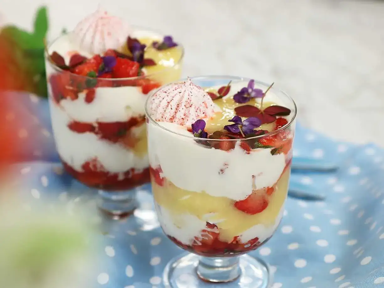 Tv&aring; glas med Eton Mess-recept: lager av gr&auml;dde, jordgubbar och mar&auml;ng, toppade med blommor.