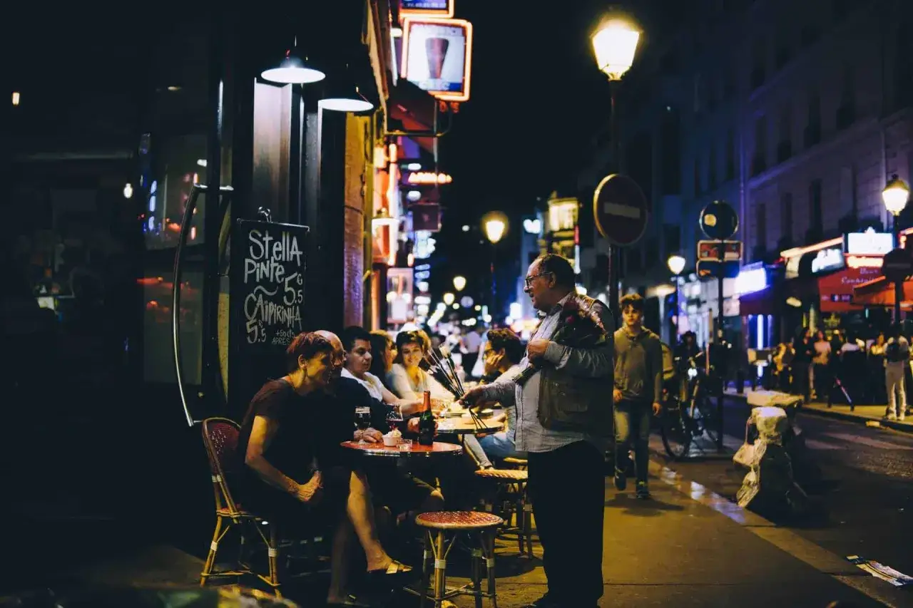 En man s&auml;ljer blommor vid ett bord utanf&ouml;r en nattklubb i Paris. Folk sitter och njuter av kv&auml;llen.