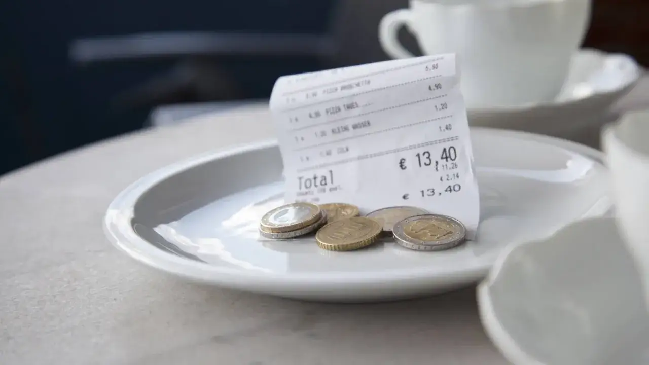 En kvitto och n&aring;gra mynt p&aring; en tallrik, redo f&ouml;r dricks i Spanien. En kaffekopp syns i bakgrunden.