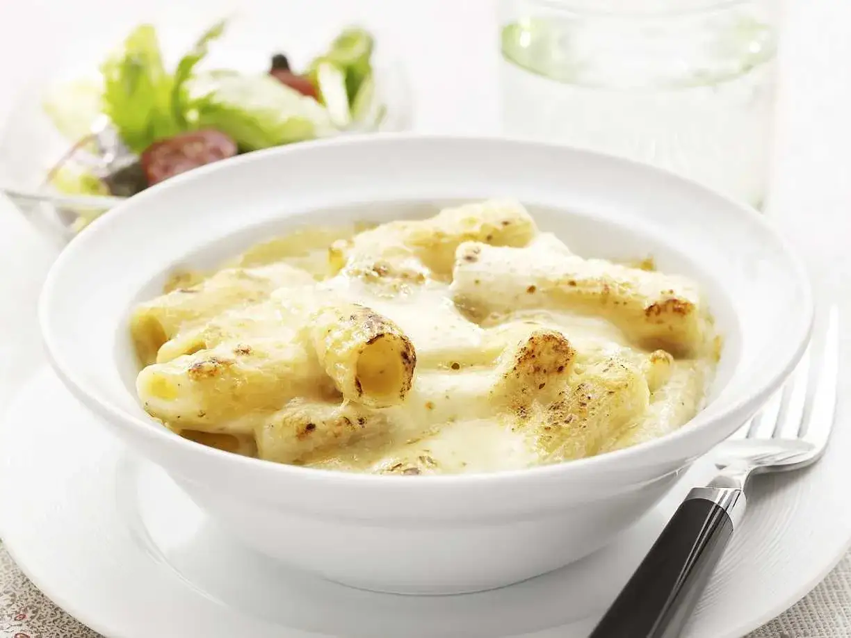 En sk&aring;l med kr&auml;mig mac and cheese, gyllene och bubblande, serverad med en fr&auml;sch sallad och ett glas vatten.