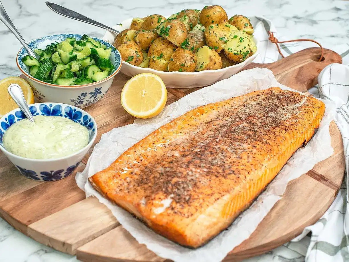 En saftig laxfil&eacute;, perfekt f&ouml;r att grilla lax, serveras med f&auml;rskpotatis, gurksallad och en kr&auml;mig s&aring;s.