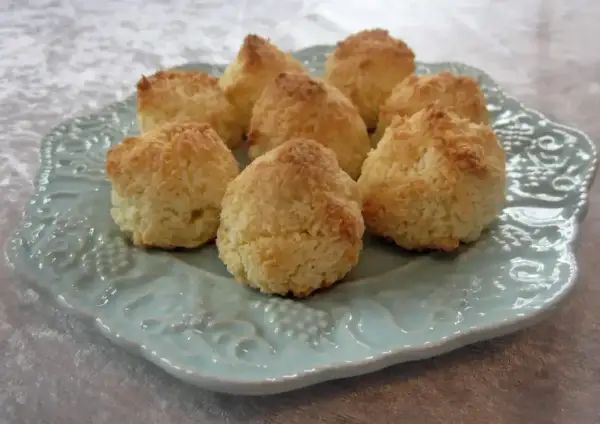 Små, gyllene kokostoppar ligger uppradade på en vacker ljusblå tallrik. Perfekta att baka med detta kokostoppar recept!