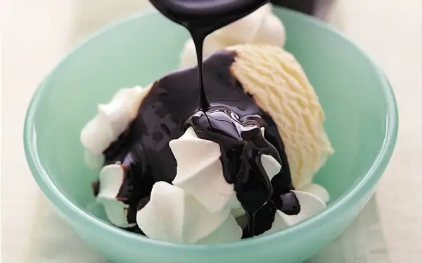 En skål med vaniljglass och visp täcks av glansig chokladsås. Ett perfekt chokladsås recept för en lyxig dessert.
