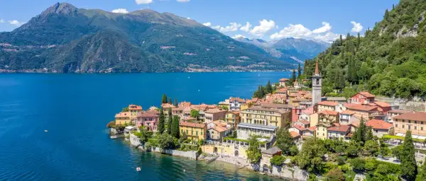 Färgstark by vid en blå sjö i norra Italien, med gröna berg i bakgrunden.
