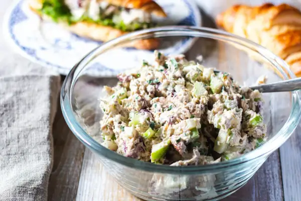 En skål med krämig kycklingsallad, perfekt för ett kycklingsallad recept. I bakgrunden syns en croissant och en smörgås.