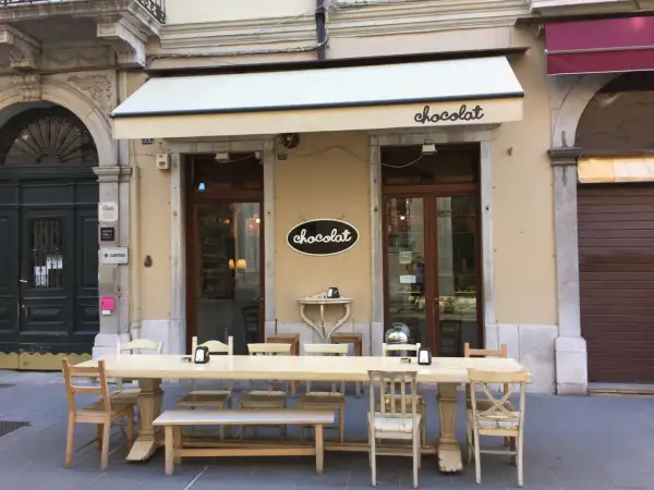 Uteservering vid ett chokladcafé i Trieste, Italien. Långt bord med stolar och bänkar framför butiken.
