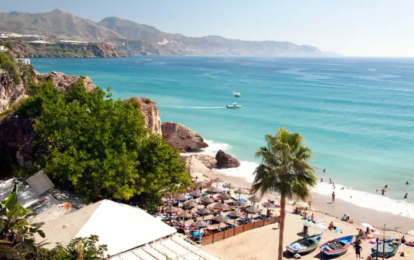 En solig strand med parasoller och badande människor. Vackert turkost hav och berg i bakgrunden. Spanien temperatur året runt är perfekt för detta.