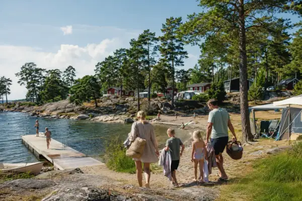 Familj på väg mot vattnet för en härlig sommarsemester med barn. Sol, bad och campingliv vid en svensk sjö.