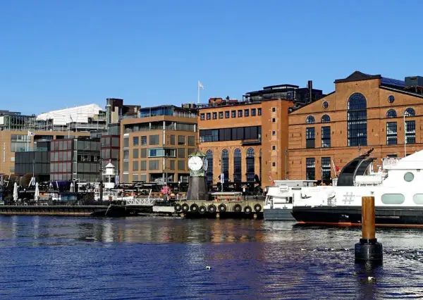 En del av Oslo med moderna byggnader, en gammal tegelbyggnad med ett stort klocktorn vid vattnet och båtar.