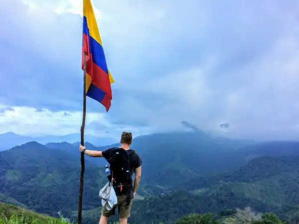 Vandrare med Colombias flagga på en bergstopp. Trots att en resa till Colombia kan verka farligt, bjuder landet på otroliga vyer.