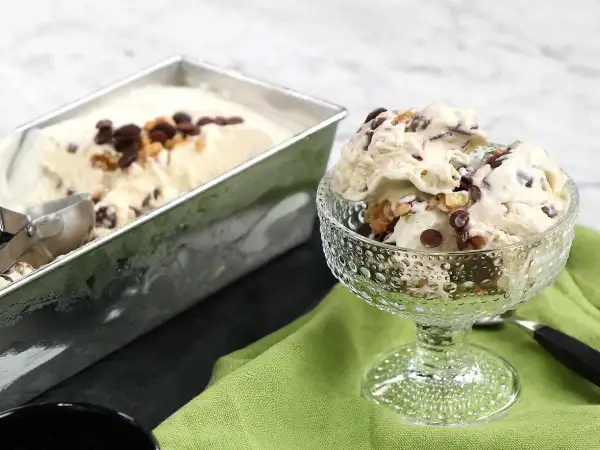 En skål med krämig nicecream banan, toppad med chokladbitar och nötter. Bredvid står en form med mer glass.
