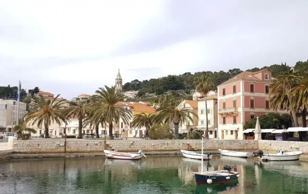 Hamnen i Hvar, Kroatien, med palmer, färgglada hus och små båtar i det turkosa vattnet.
