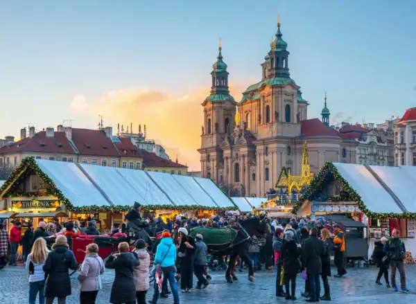 En livlig prag julmarknad med folk, häst och vagn, och en kyrka i bakgrunden.