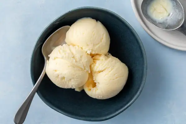 Tre skopor krämig vaniljglass i en mörkblå skål med en sked. Perfekt för ett enkelt gelato recept.
