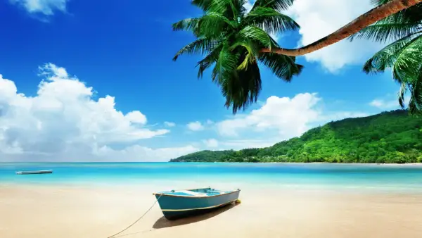 En blå båt på en sandstrand med palmer och turkost vatten. En dröm om Maldiverna eller Mauritius.