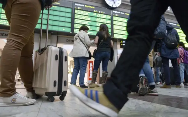 Resenärer med bagage vid en avgångstavla. Kanske dags att fundera på ving av och ombokningsskydd för resan.