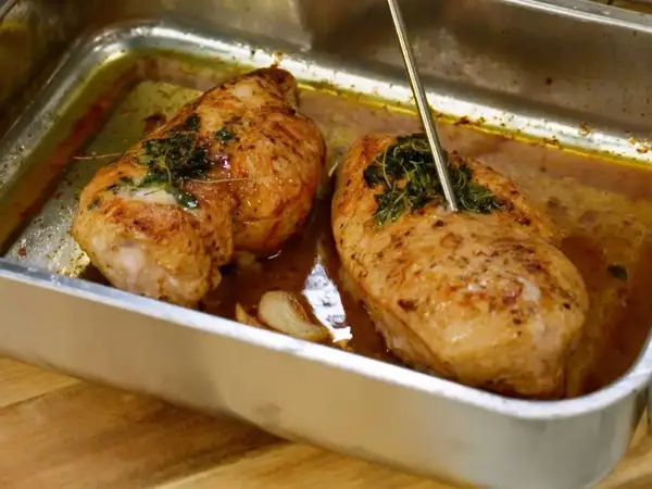Två saftiga kycklingfiléer i en ugnsform, redo att dras isär till pulled chicken. En termometer mäter temperaturen.