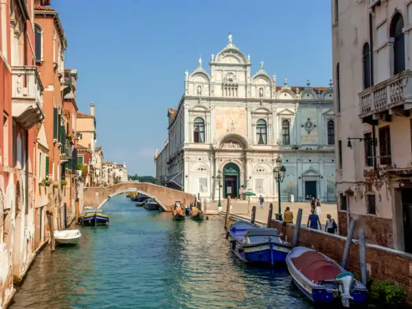 En vacker vy av en del av Venedig med kanaler, broar och historiska byggnader. Båtar ligger förtöjda längs kanalen.
